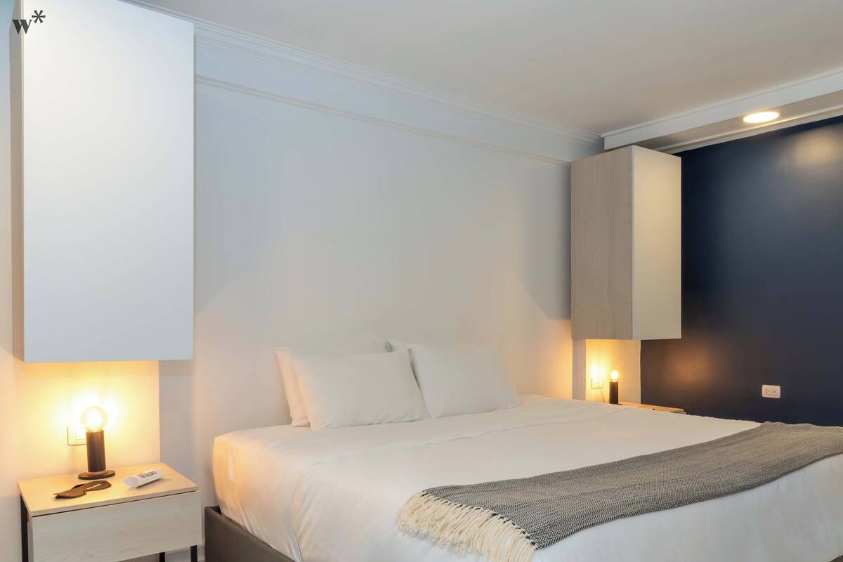 Un dormitorio moderno con cama, mesitas de noche y velador.
