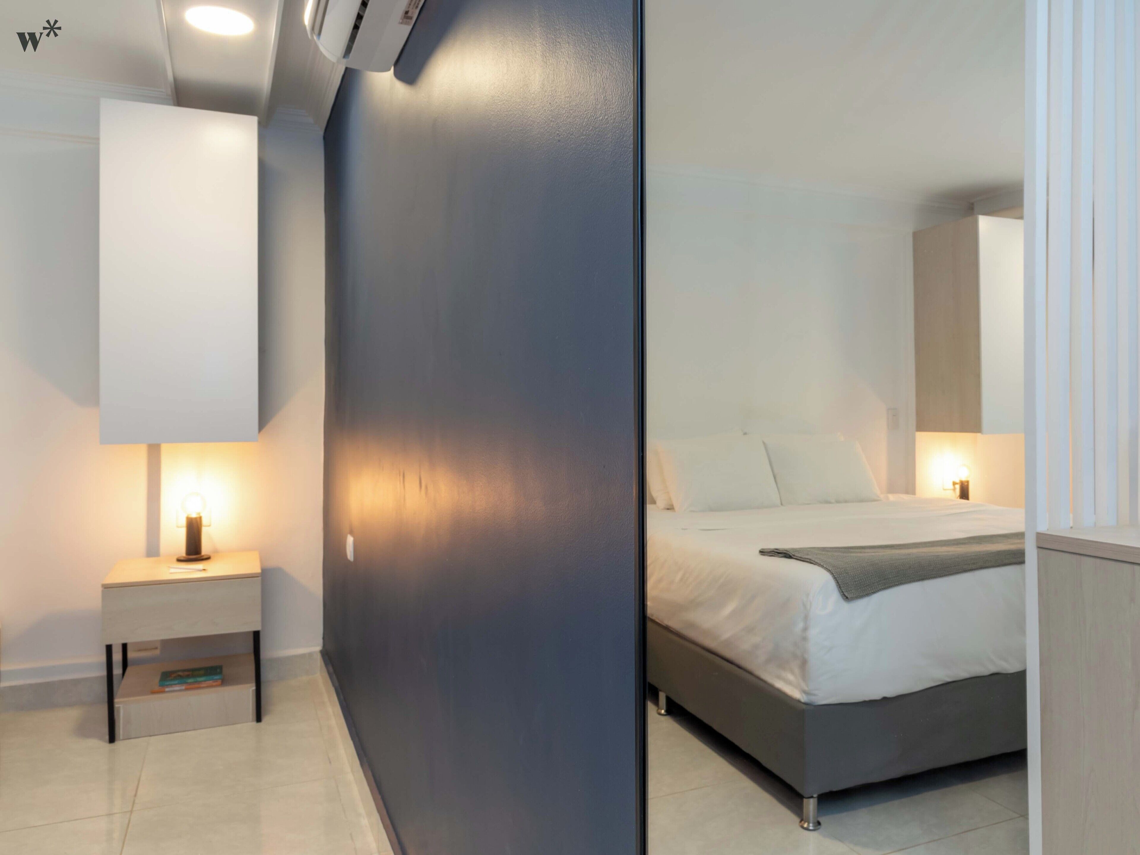 A modern bedroom with a bed, bedside tables, and a wall-mounted light fixture.