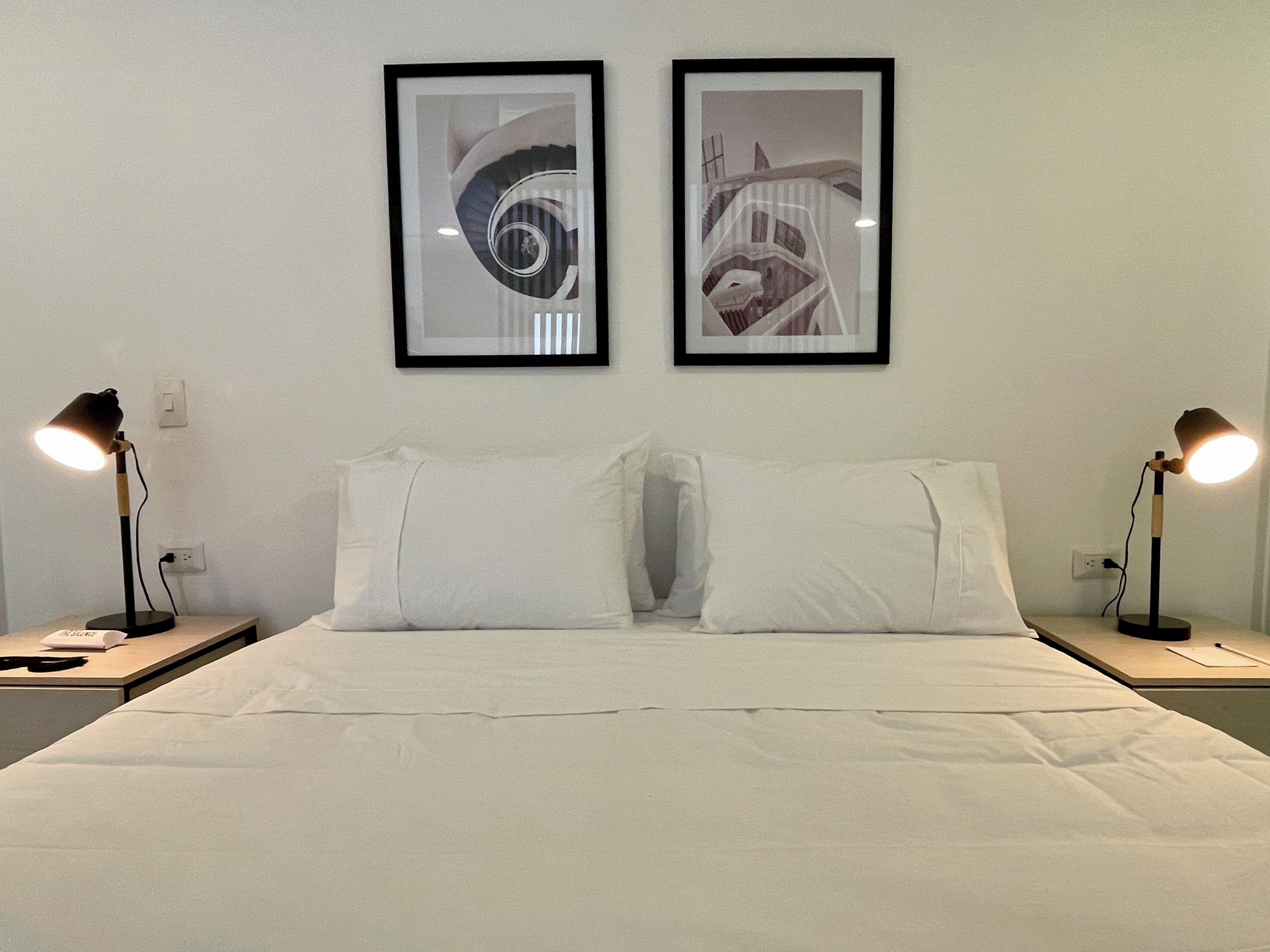 A hotel room with a large bed, two nightstands, two framed pictures on the wall, and two bedside lamps.