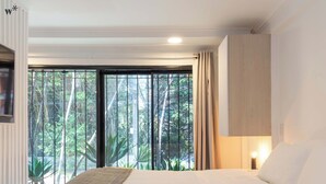 A bedroom with a large bed, a view of greenery through the window, and a ceiling light. - Lalinde by Wynwood House (Medellín)