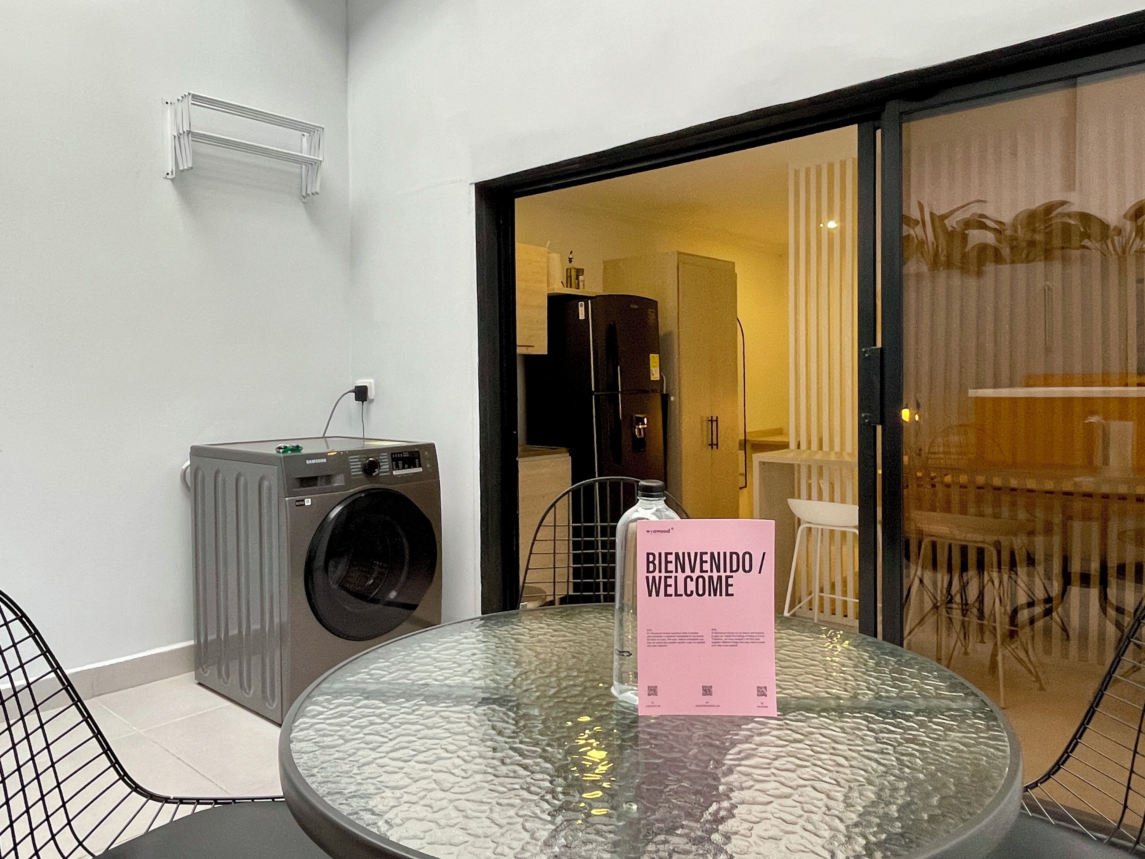 A modern room with a glass table, a washing machine, and a welcome sign.