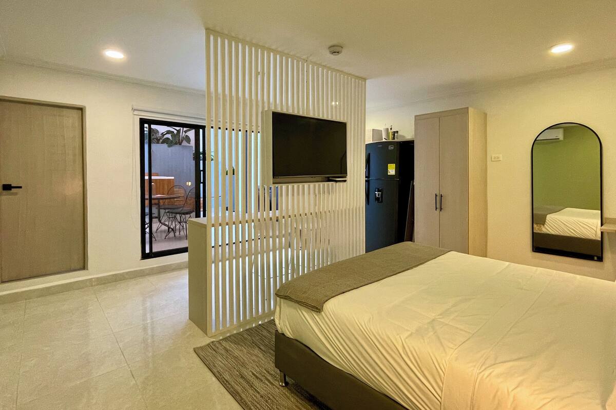 Un dormitorio moderno con una cama grande, un televisor montado en la pared y un refrigerador.