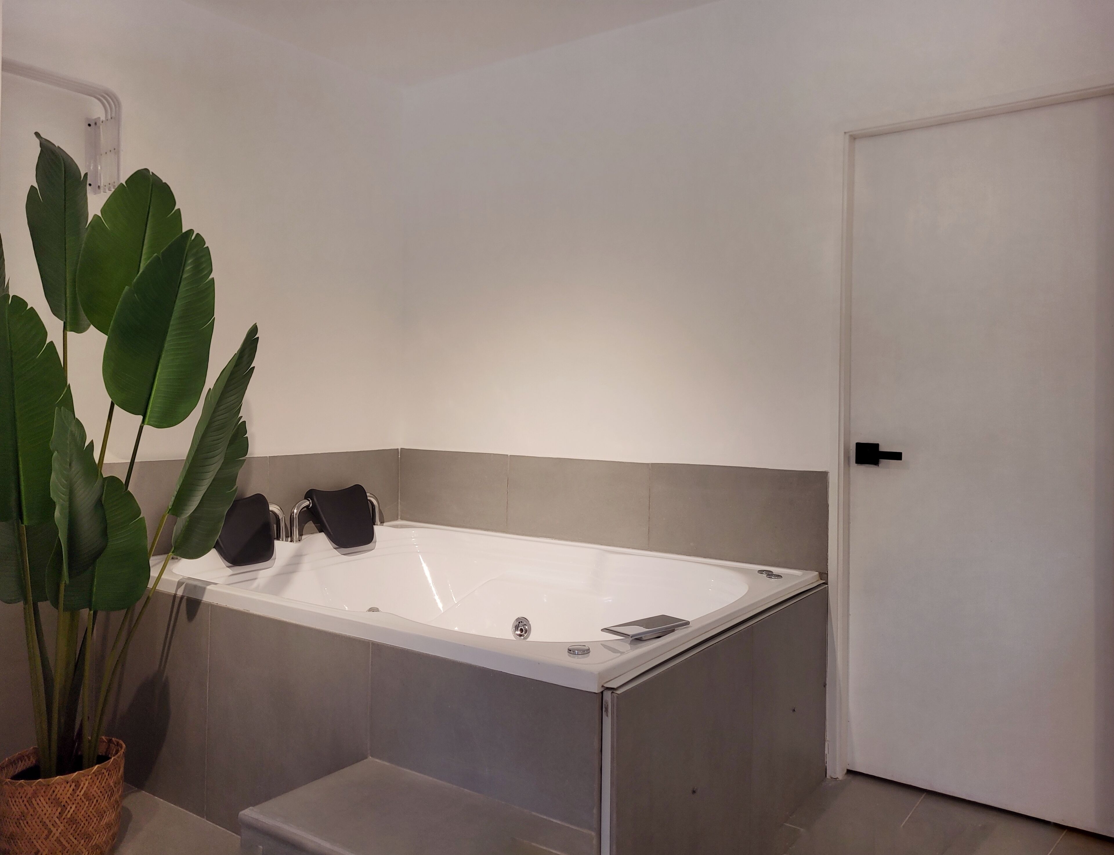 A modern bathroom with a white bathtub, grey tiles, and a potted plant.
