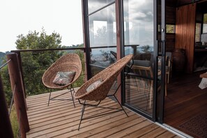 A wooden deck with wicker chairs and a glass door leading to an interior space. - Owl's Watch Nature Retreat (Manizales)