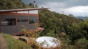 A modern house with a hot tub on a deck, surrounded by dense forest and hills. - Owl's Watch Nature Retreat (Manizales)