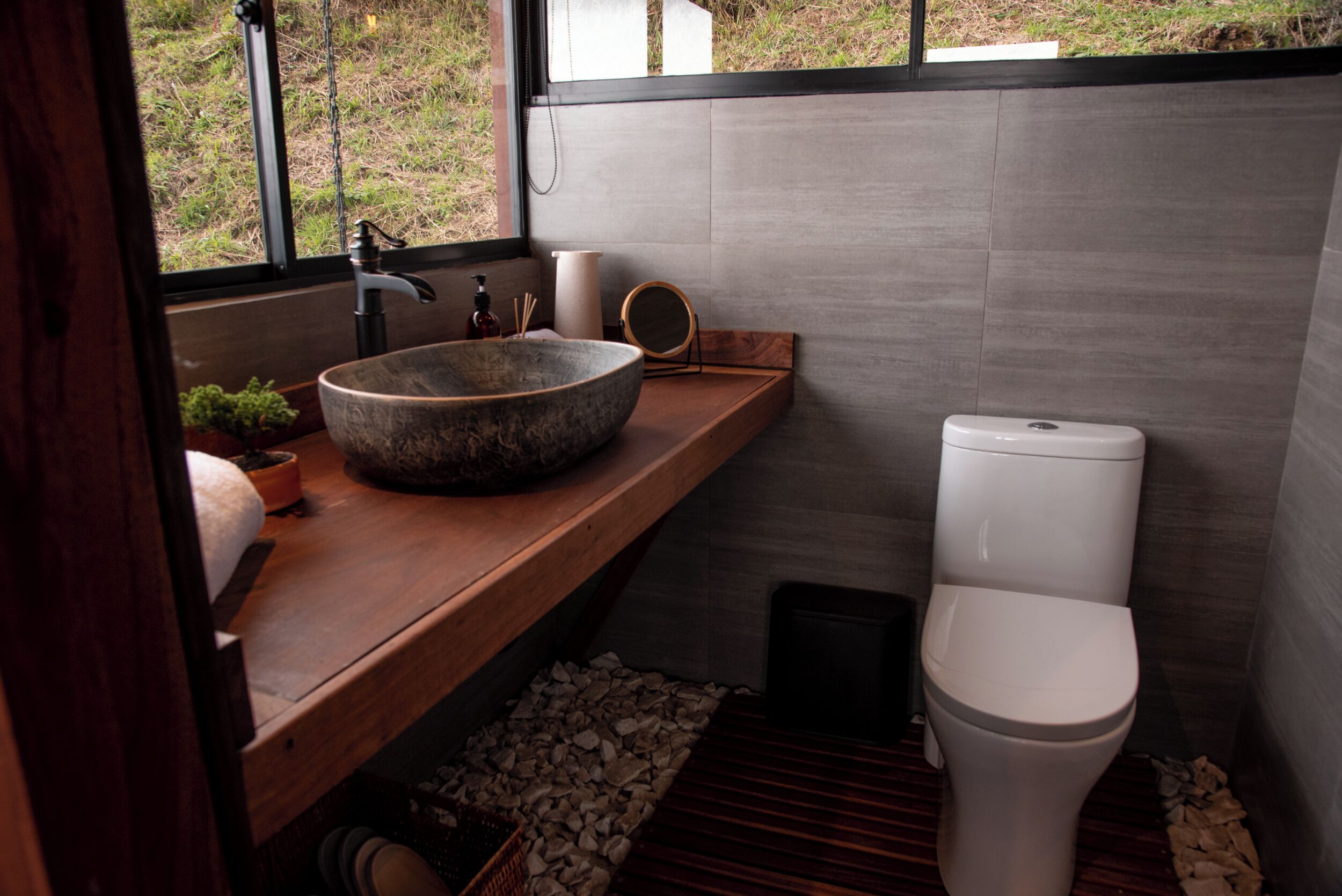 Un baño moderno con un lavamanos grande de piedra, encimera de madera y un inodoro blanco.