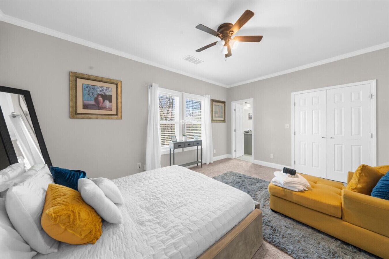 Une chambre à coucher avec un lit, un canapé jaune, un ventilateur de plafond et une porte donnant sur une salle de bain.