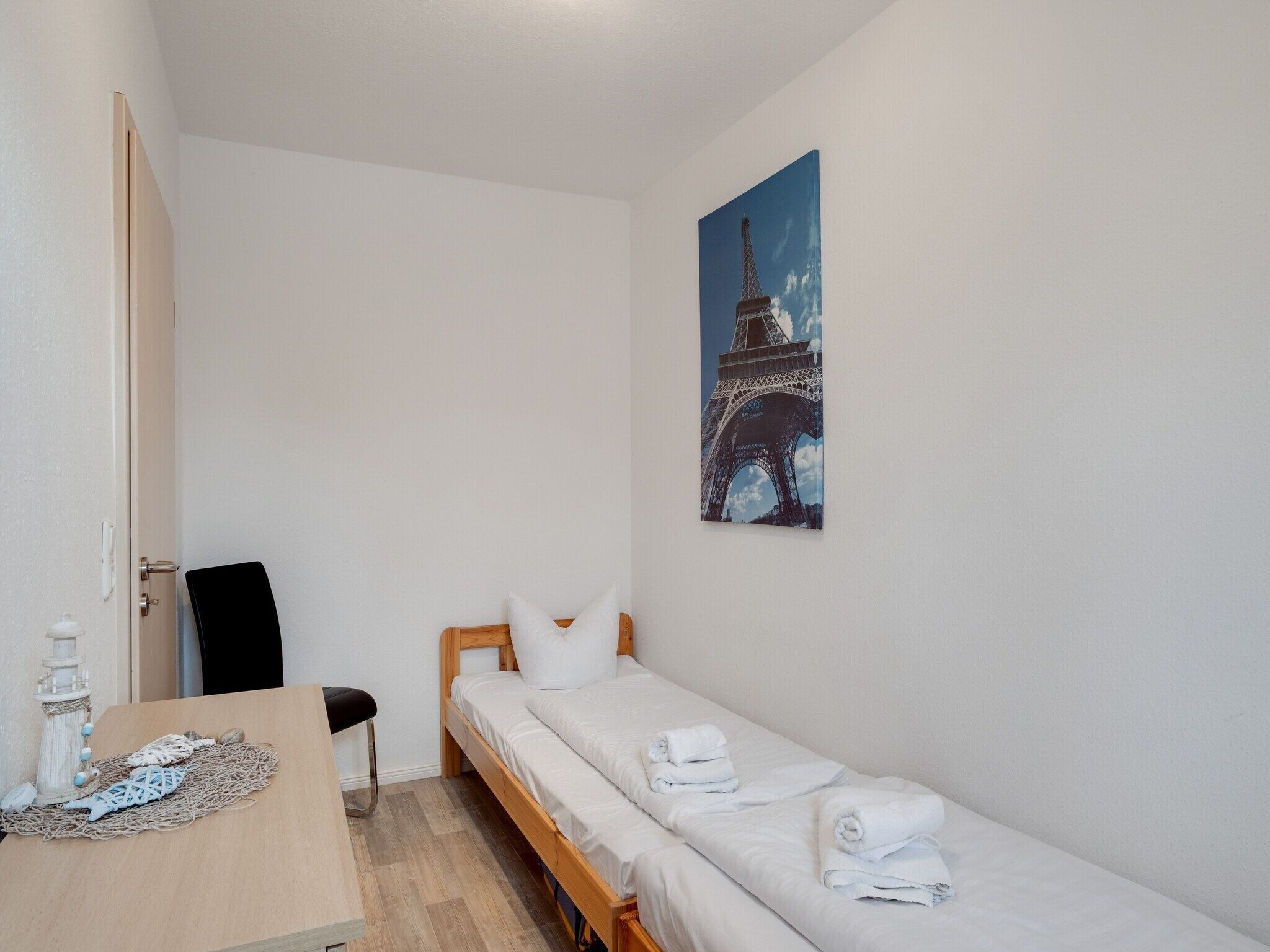 Ein kleiner, sauberer Raum mit einem Bett, einem Sessel, einem Tisch und einem Bild des Eiffelturms.