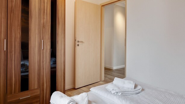 Hotellihuone, jossa on puinen vaatekaappi, suljettu ovi ja kaksi sänkyä, joissa on pyyhkeet.