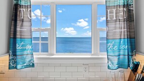 A window with curtains displaying "TO" and "HE" on them, overlooking a clear blue sky and ocean. - Lighthouse Retreat Close to Lambeau Field
and the amazingDoor county Fall Color (Algoma)