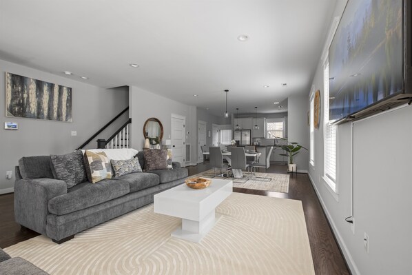 A modern living room with a gray sofa, white coffee table, and a large abstract painting on the wall. - Downtown RVA Cozy 3BR Near VCU (Richmond)