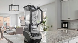 A kitchen with a Ninja blender on the counter, a dining area with a table and chairs, and a view of a brick building through the window. - Spacious Duplex, Near VCU, 5 Free Parking, Fenced (Richmond)