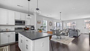 A modern kitchen with white cabinets, a large island, and a dining area with a gray couch and chairs. - Spacious Duplex, Near VCU, 5 Free Parking, Fenced (Richmond)