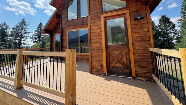 Una cabaña de madera con terraza, ventanas grandes y vistas a la montaña.