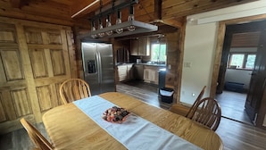 Un comedor de madera con una mesa preparada para dos personas, un refrigerador y una cocina al fondo.