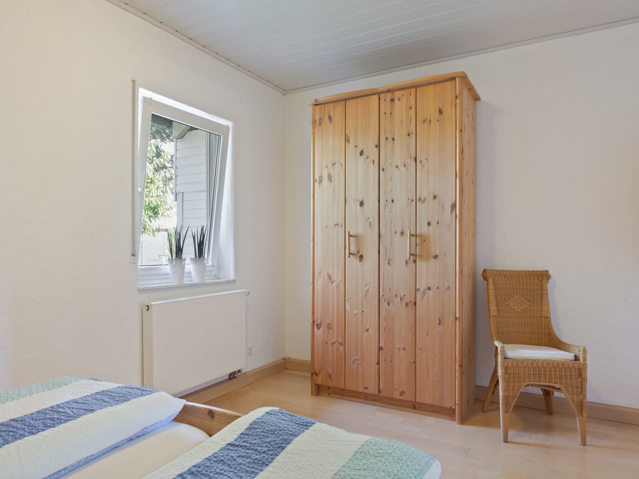 Une chambre avec une armoire en bois, une chaise en osier et une fenêtre ornée de plantes.
