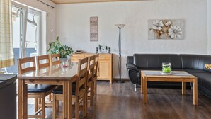 A modern living room with a wooden dining table, black leather sofa, and a floor lamp.