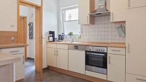 A modern kitchen with white cabinets, a stainless steel oven, and a window with blinds.
