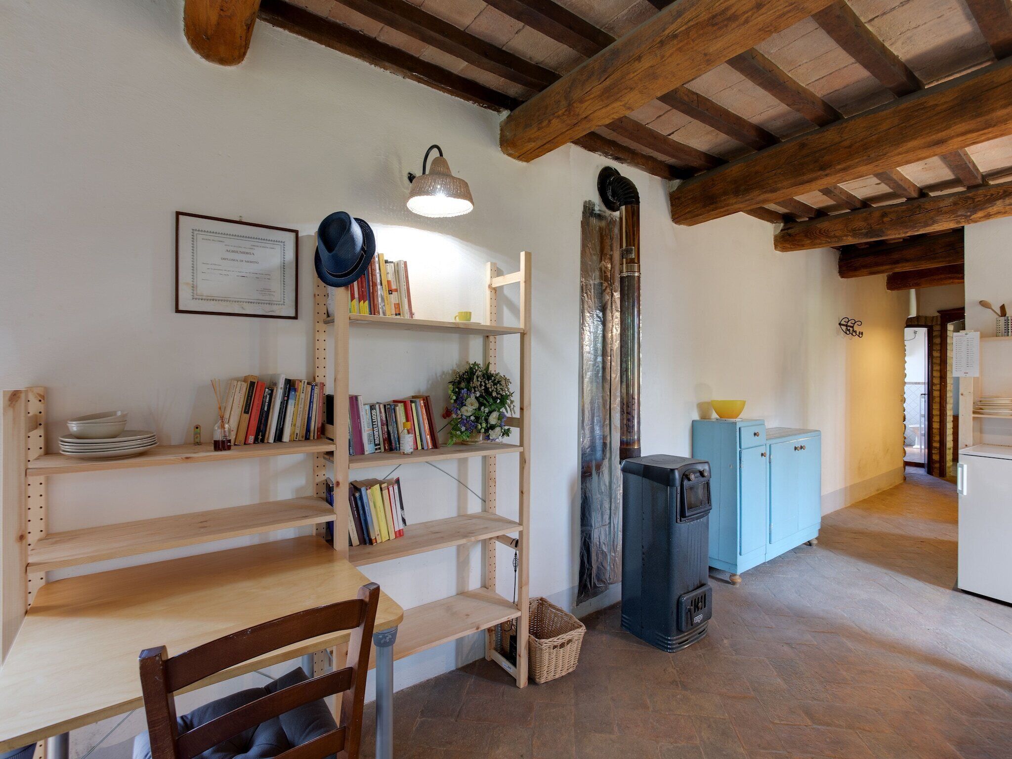 Habitació acollidora amb bigues de fusta, una prestatgeria, una taula, una cadira, una cuina i un petit armari.