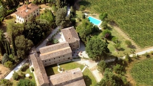 Une vue aérienne d’un grand bâtiment à plusieurs ailes, entouré d’une végétation luxuriante et de vignobles.