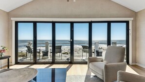 Une pièce spacieuse dotée d’une grande porte-fenêtre coulissante donnant sur un balcon avec vue sur la plage.
