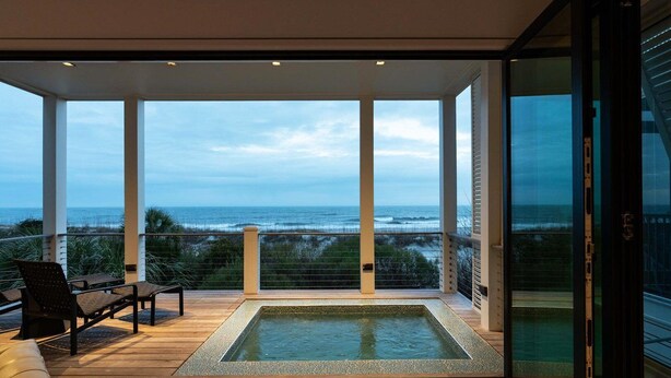 Un balcon moderne avec vue sur l’océan, une petite piscine et deux chaises.