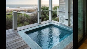 Un jacuzzi rectangulaire installé sur une terrasse en bois, offrant une vue sur l’océan.