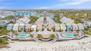 Un hôtel situé en bord de mer, composé de plusieurs bâtiments aux couleurs vives, doté d’une piscine centrale et d’une zone de plage aménagée avec des parasols.