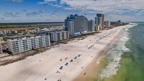Un hôtel situé sur la côte, composé de plusieurs immeubles de grande hauteur, avec une plage de sable et une jetée qui s’avance dans l’eau.