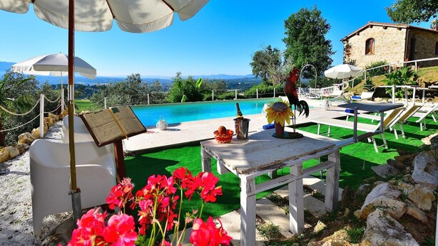 A poolside area with lounge chairs, a table, and a view of the sea.