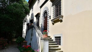 A building with a stone staircase leading to a door, surrounded by potted plants and a gravel path.