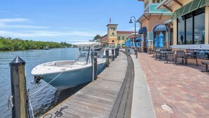 A waterfront dock with boats, a restaurant with outdoor seating, and a building with a tower.