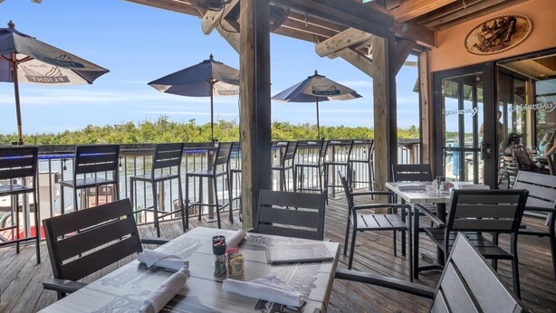 An outdoor dining area with wooden tables and chairs, umbrellas, and a view of the water.