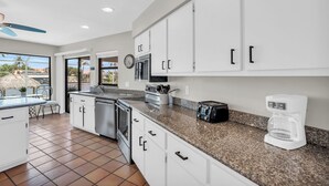 A modern kitchen with white cabinets, granite countertops, a built-in oven, a microwave, and a coffee maker.