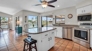 A spacious kitchen with a central island, stainless steel appliances, and large windows offering views of palm trees.