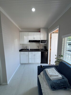 A compact kitchen with white cabinets, a black countertop, and a microwave.