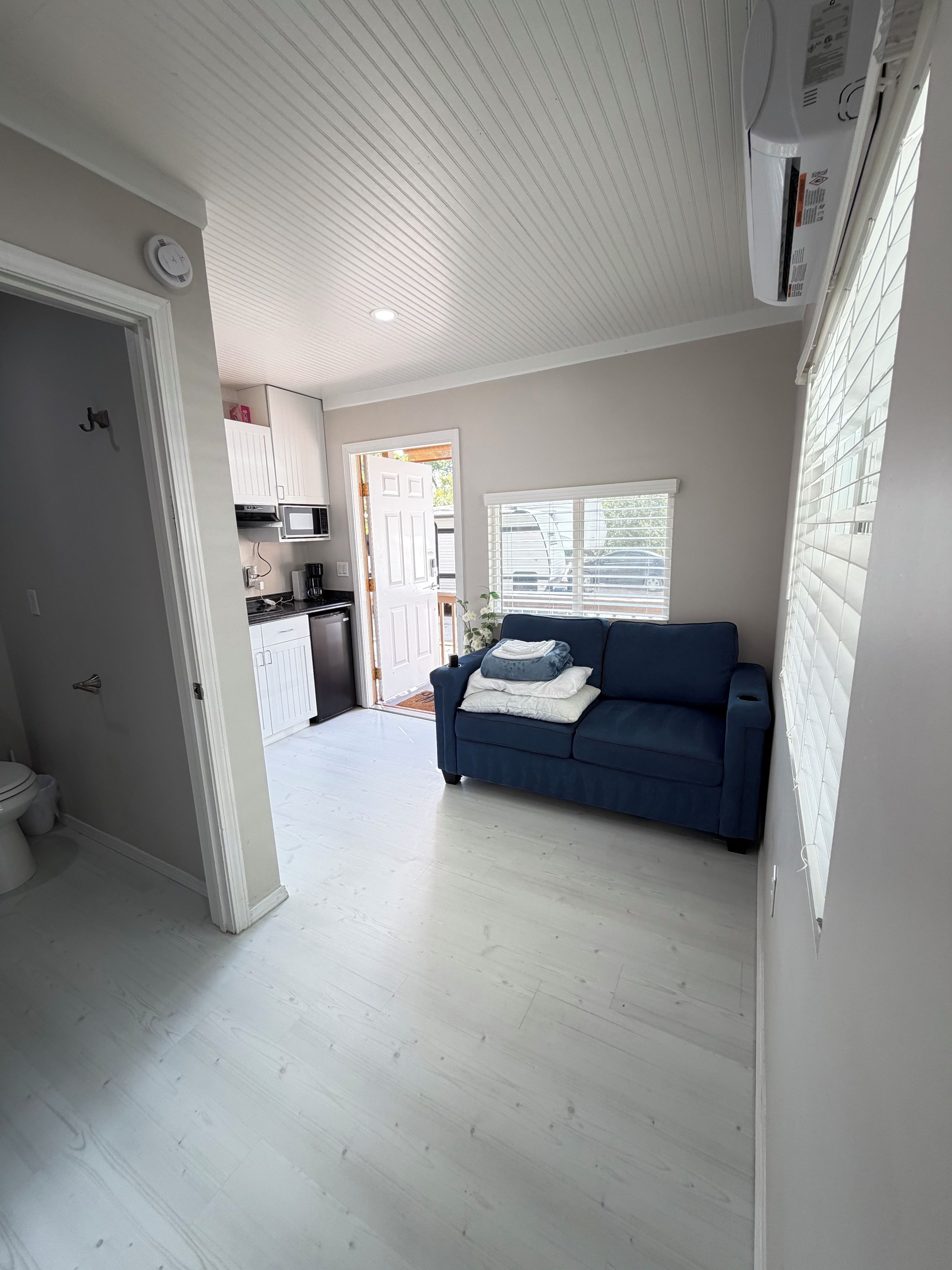 Een moderne woonkamer met een blauwe bank, een witte deur en een keuken in de achtergrond.