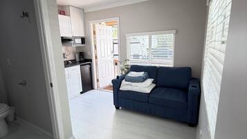 Een moderne woonkamer met een blauwe bank, een witte deur en een keuken in de achtergrond.