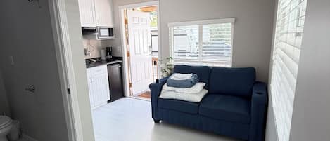 Un salon moderne avec un canapé bleu, une porte blanche et un coin cuisine à l’arrière-plan.