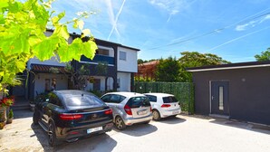 A residential area with two parked cars, a house with a balcony, and a small shed.