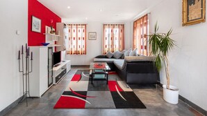 Ein modernes Wohnzimmer mit Sofa, Couchtisch und Essbereich mit Fernseher. Vorhanden sind Vorhänge, eine Pflanze und ein Gemälde an der Wand.