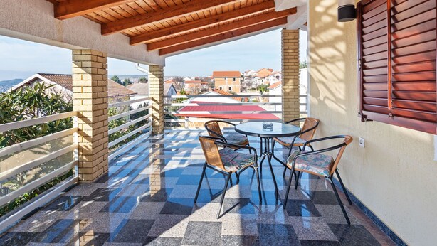 A covered outdoor patio with a table and chairs, a view of buildings in the distance, and a wooden ceiling. - Holiday Home in Jasenice near Maslenica Beach (JASENICE)