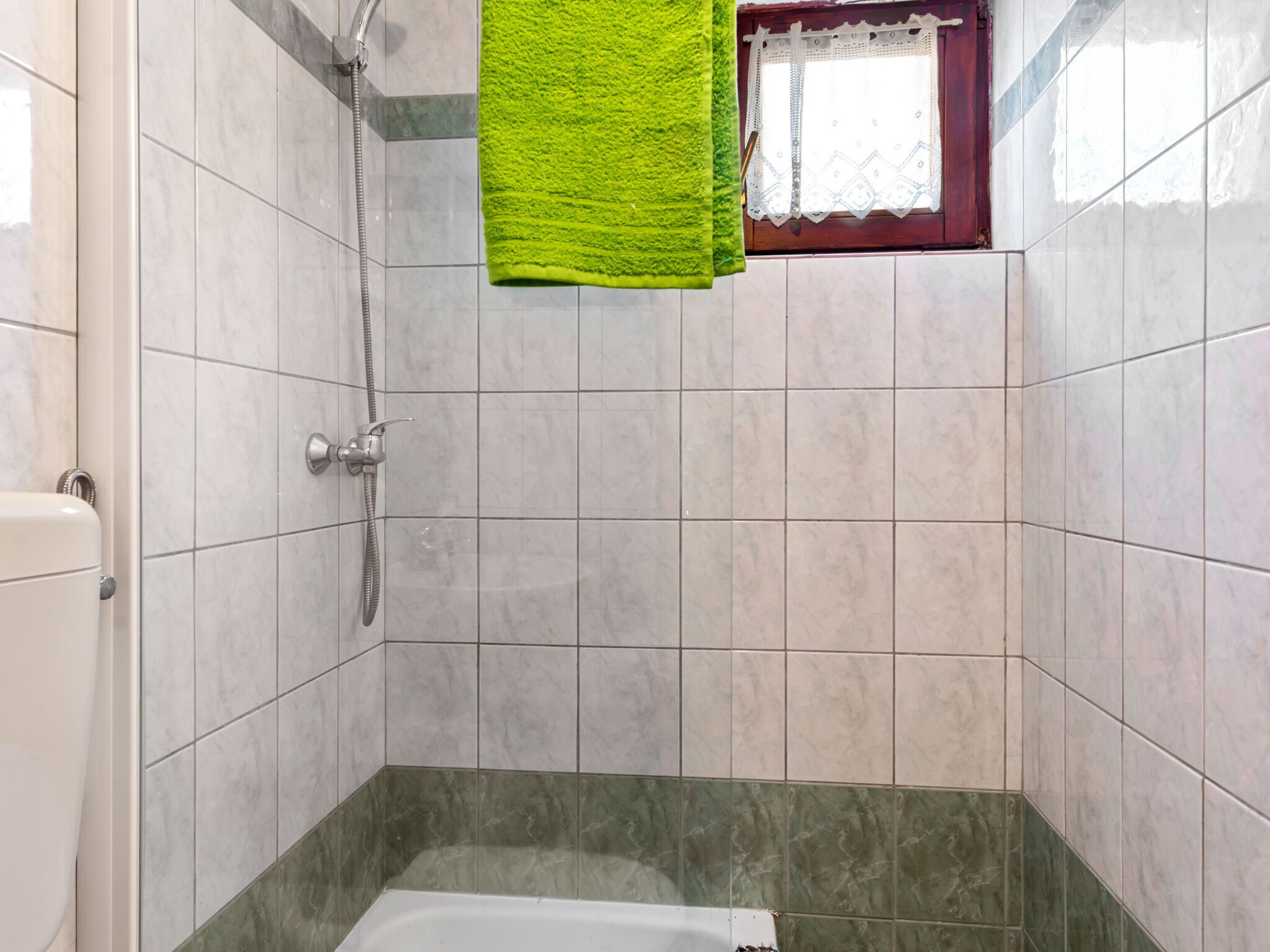 A bathroom with a shower, a bathtub, and a window with lace curtains.