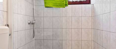 A bathroom with a shower, a bathtub, and a window with lace curtains.