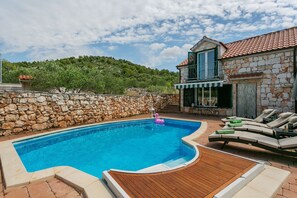 A swimming pool with a wooden deck, lounge chairs, and a stone wall.