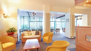 Eine geräumige Lobby mit Korbmöbeln, großen Fenstern und Blick ins Freie.
