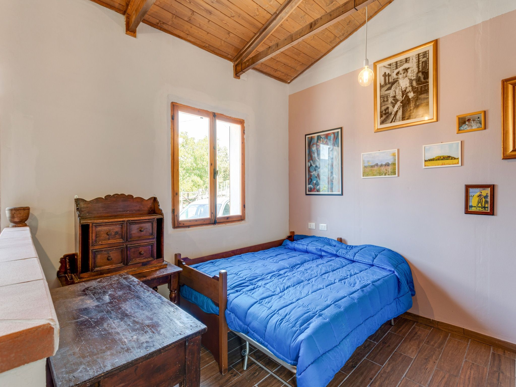 Una habitación con una cama, un aparador de madera, una mesa y una ventana.