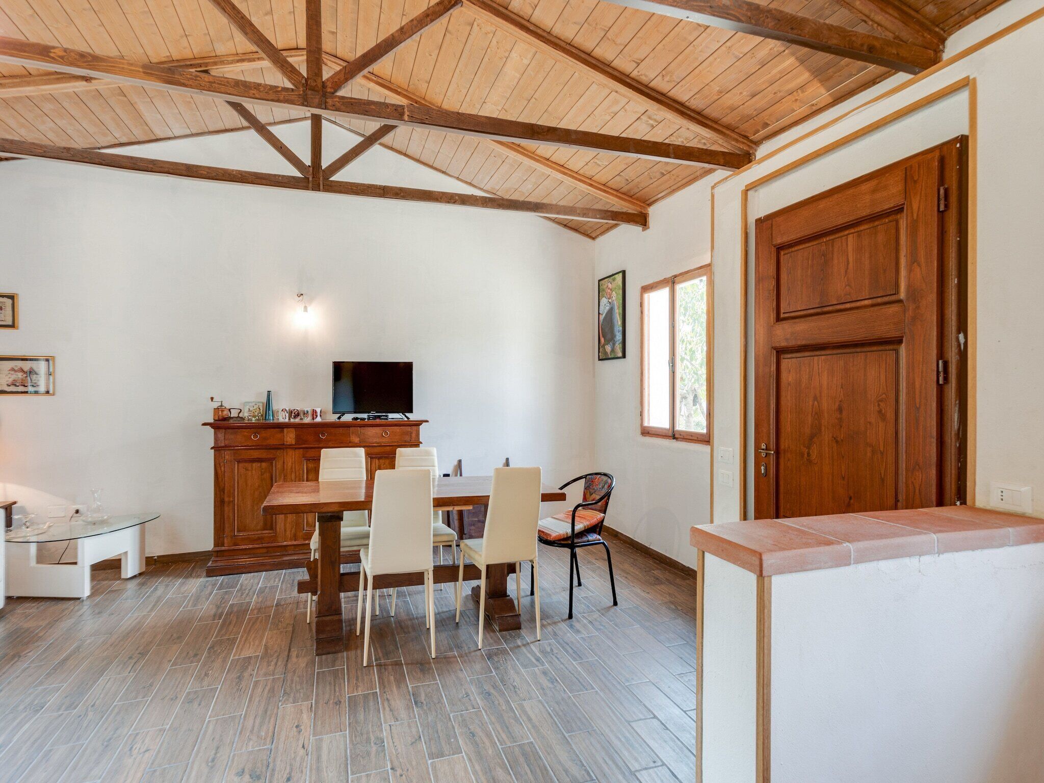 A dining area with a wooden ceiling, a TV on a wooden cabinet, and a window with a view.