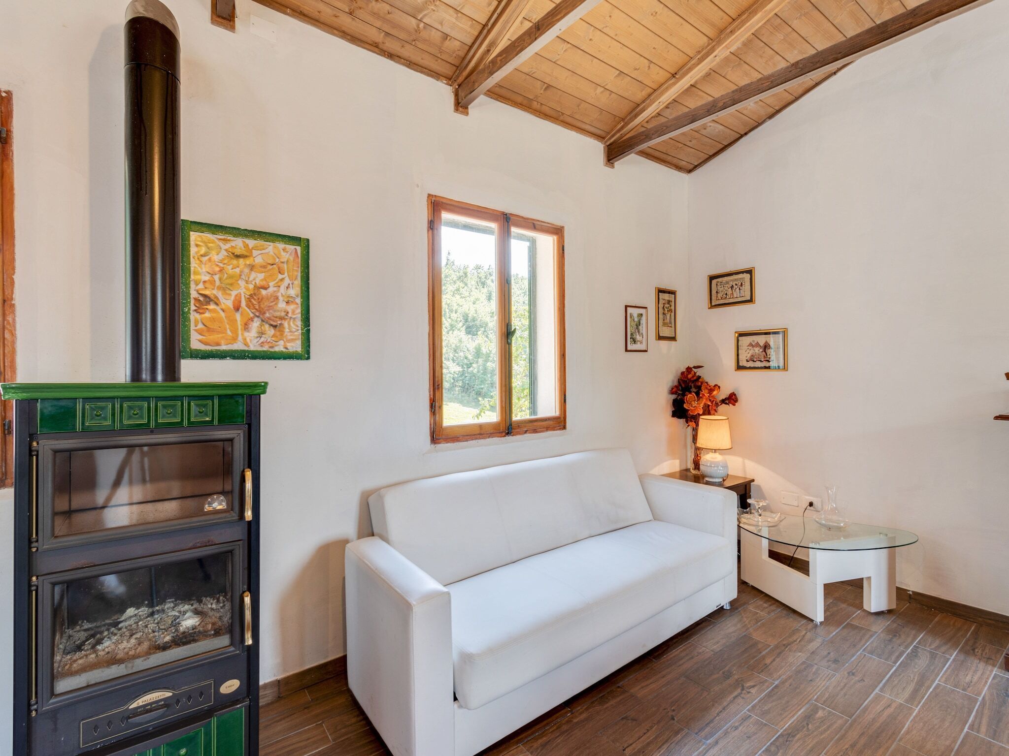 A room with a white sofa, a small table with a lamp, a fireplace with a green mantel, and framed pictures on the wall.