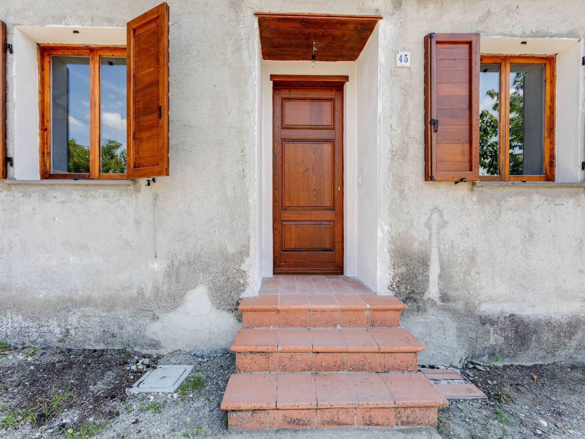 A building with a wooden door, two windows with wooden shutters, and a small set of steps leading to the entrance.